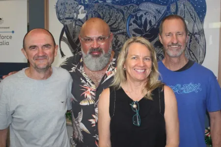 Four smiling people standing together in front of blue painting
